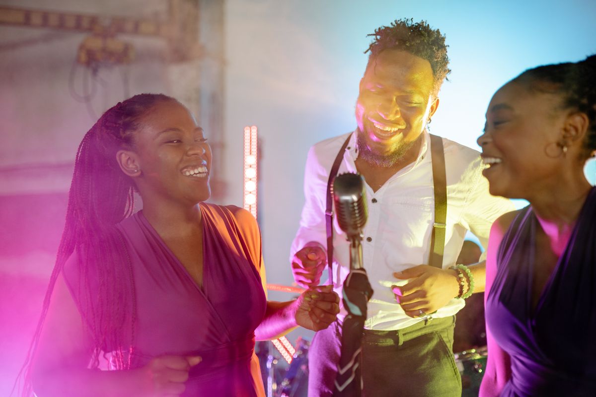 Three live singers sharing a microphone under stage lighting